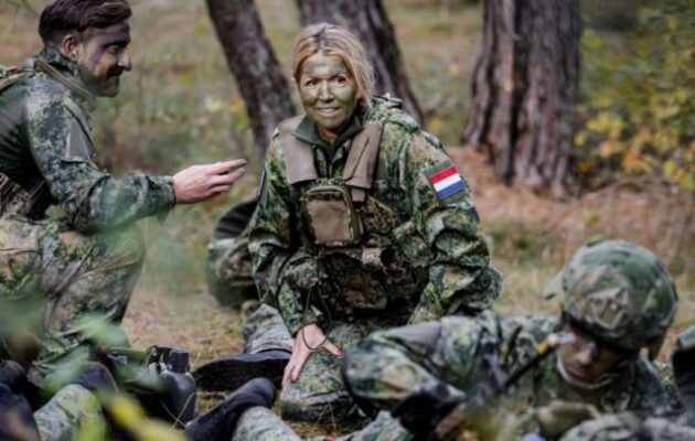 Η βασίλισσα Μάξιμα της Ολλανδίας με στολή παραλλής και φούμο στο πρόσωπο σε στρατιωτική άσκηση